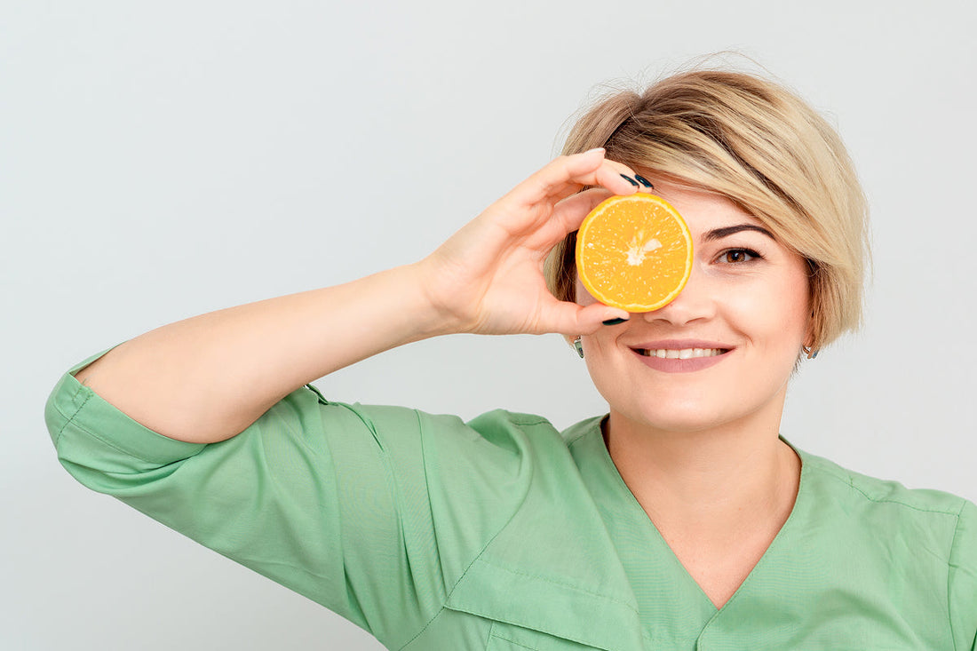 blond woman holding orange in front of her eye