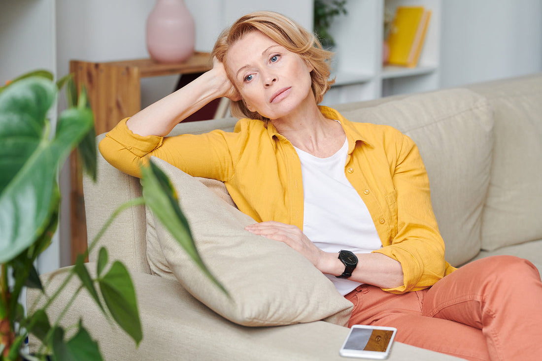 adult woman overthinking sitting on couch in living room wearing colorfull clothing
