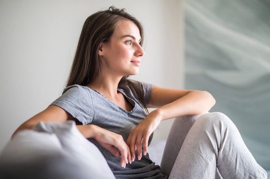 young woman sitting on a couch leaning on her knees, grey clothing