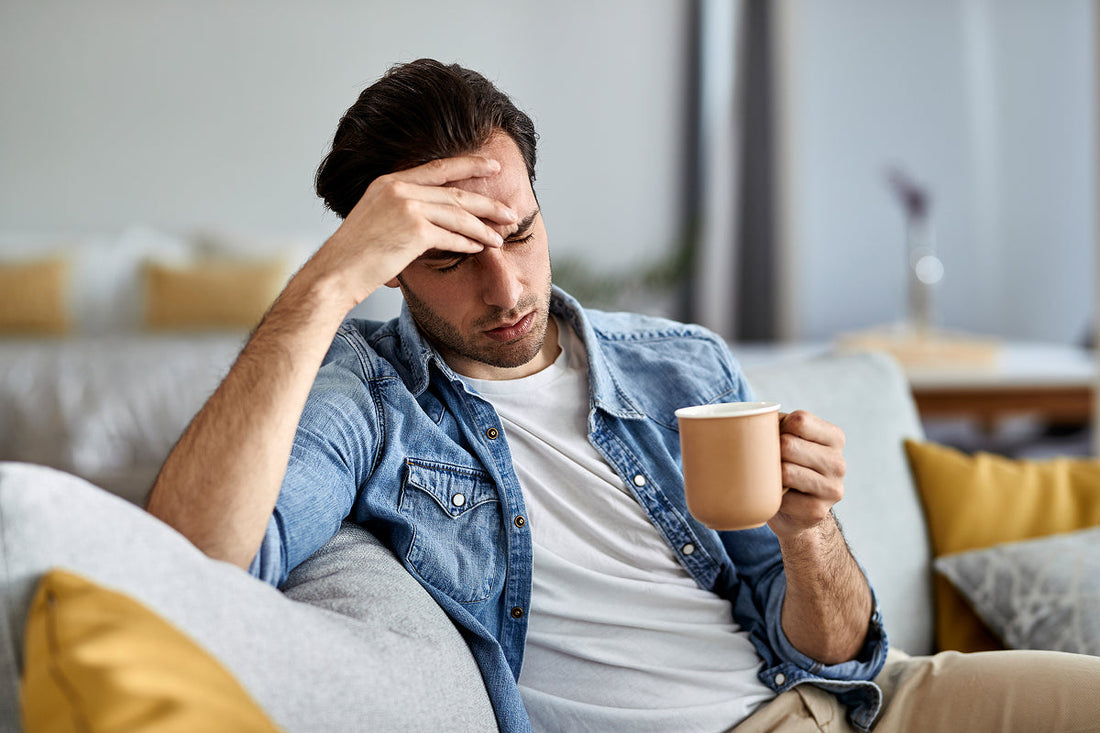 man sitting on sofa with coffee holding hand on his head