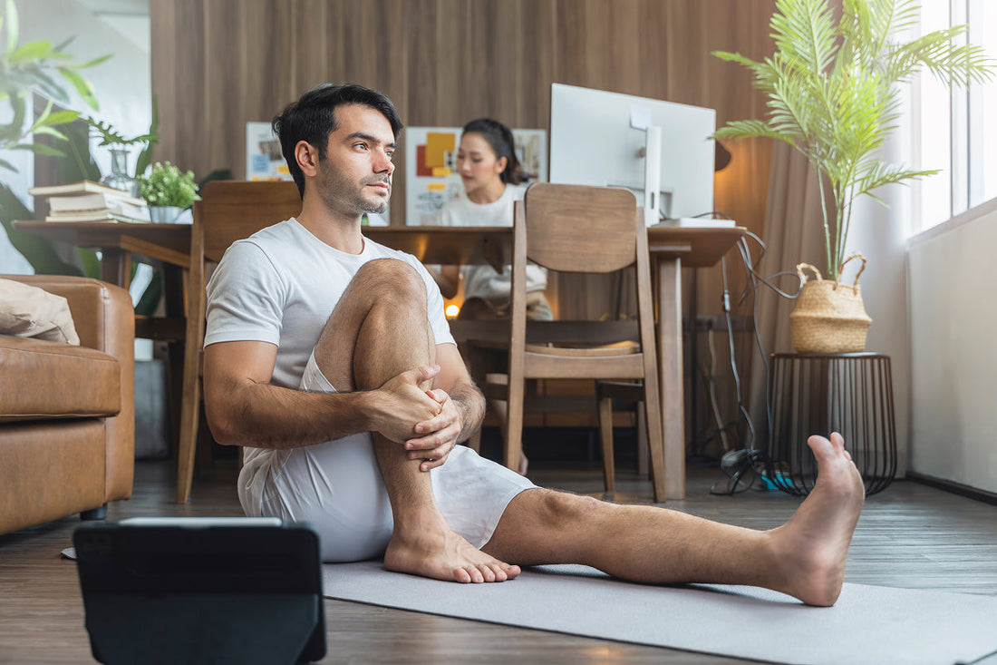 man stretching legs sitting on ground, woman working on computer in the background