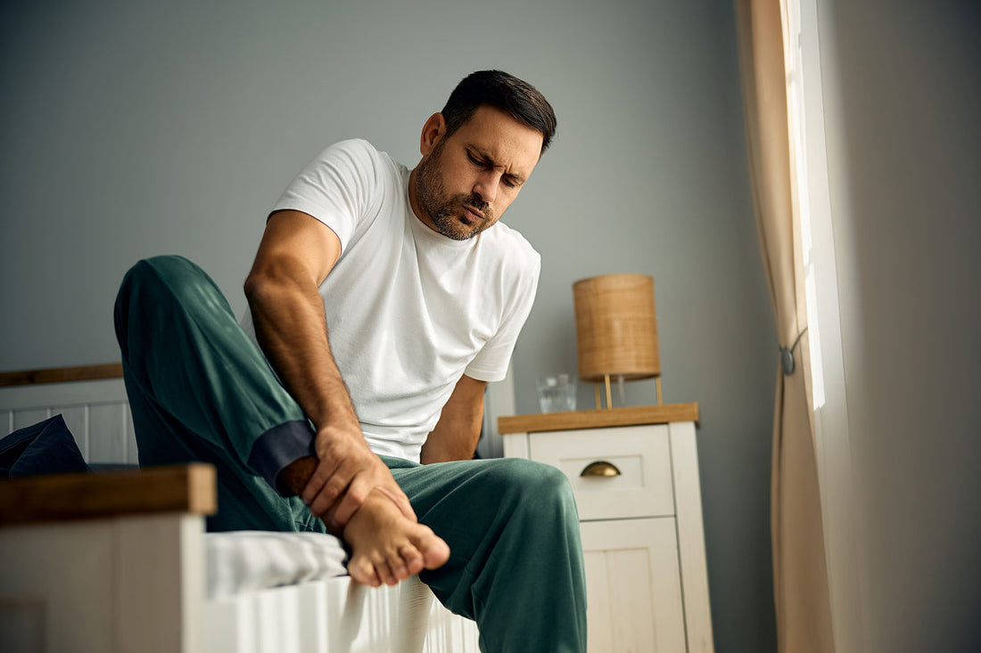 man holding foot while sitting on edge of bed