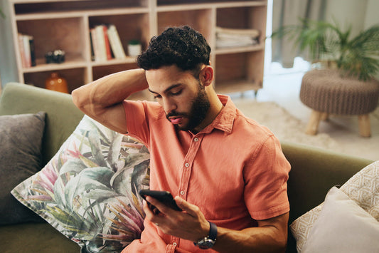 man holding head and watching phone on couch in living room