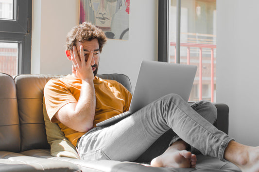 Man sitting on couch with laptop on lap holding hand over head