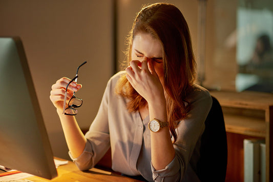 woman tired behind desk with computer holding glasses