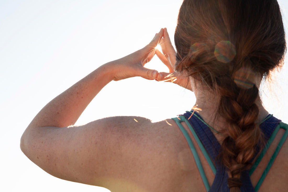 over shoulder view of woman with braided hair in sporty clothes holding hands with the sun shining trough