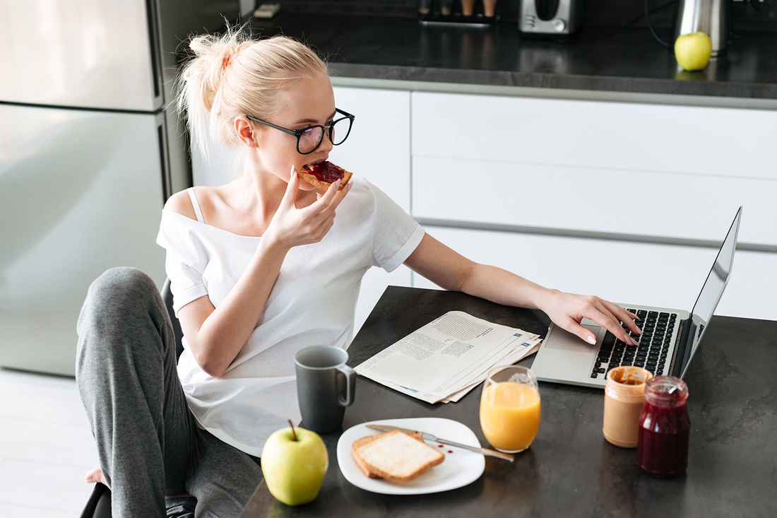 Woman eating breakfast while working on her laptop