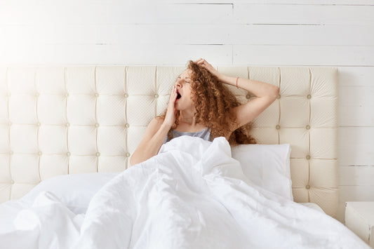 red hair curly woman waking up, yawning, in a white bed